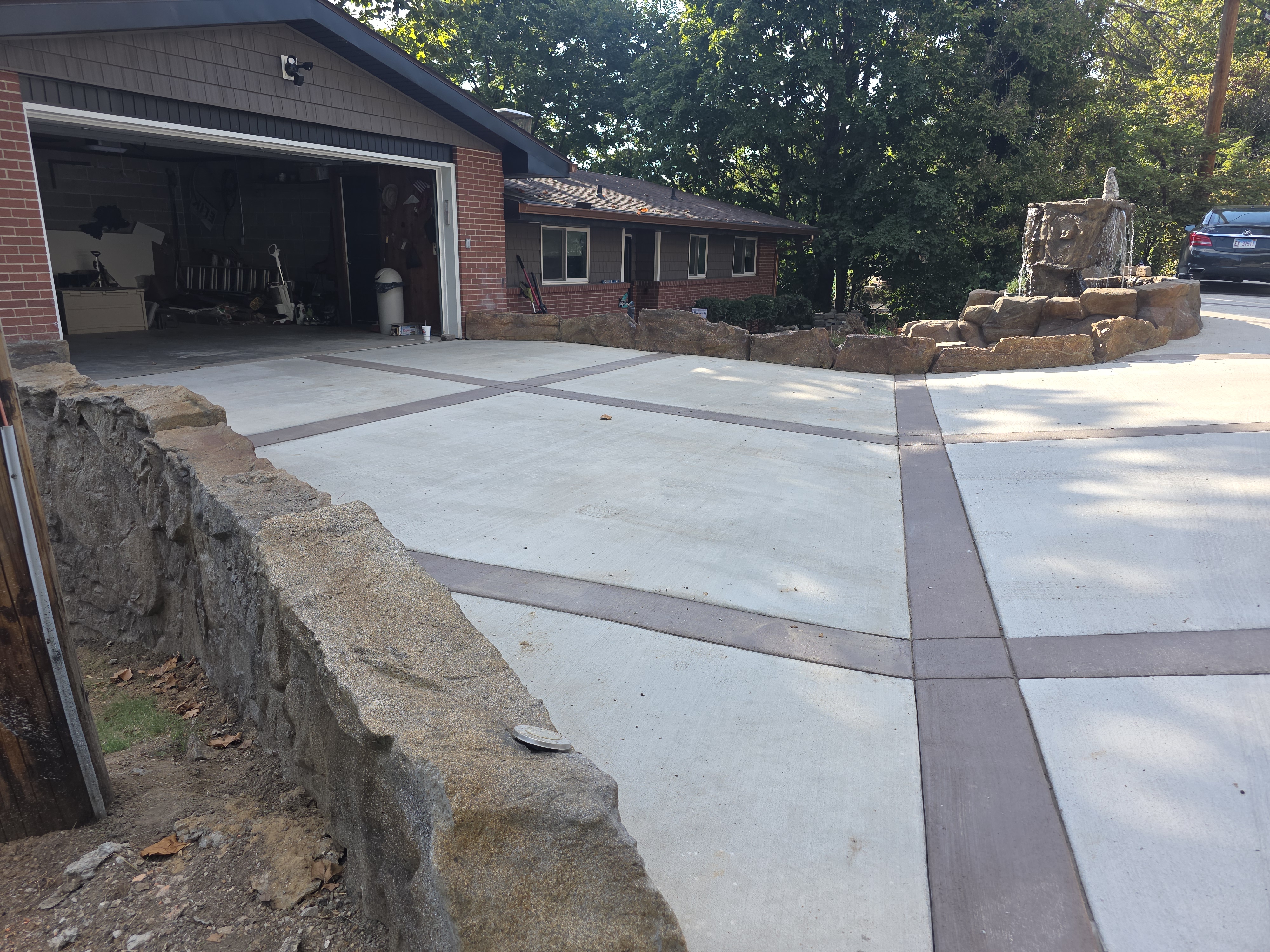 Decorative concrete driveway with colored bands beside a carved stone wall