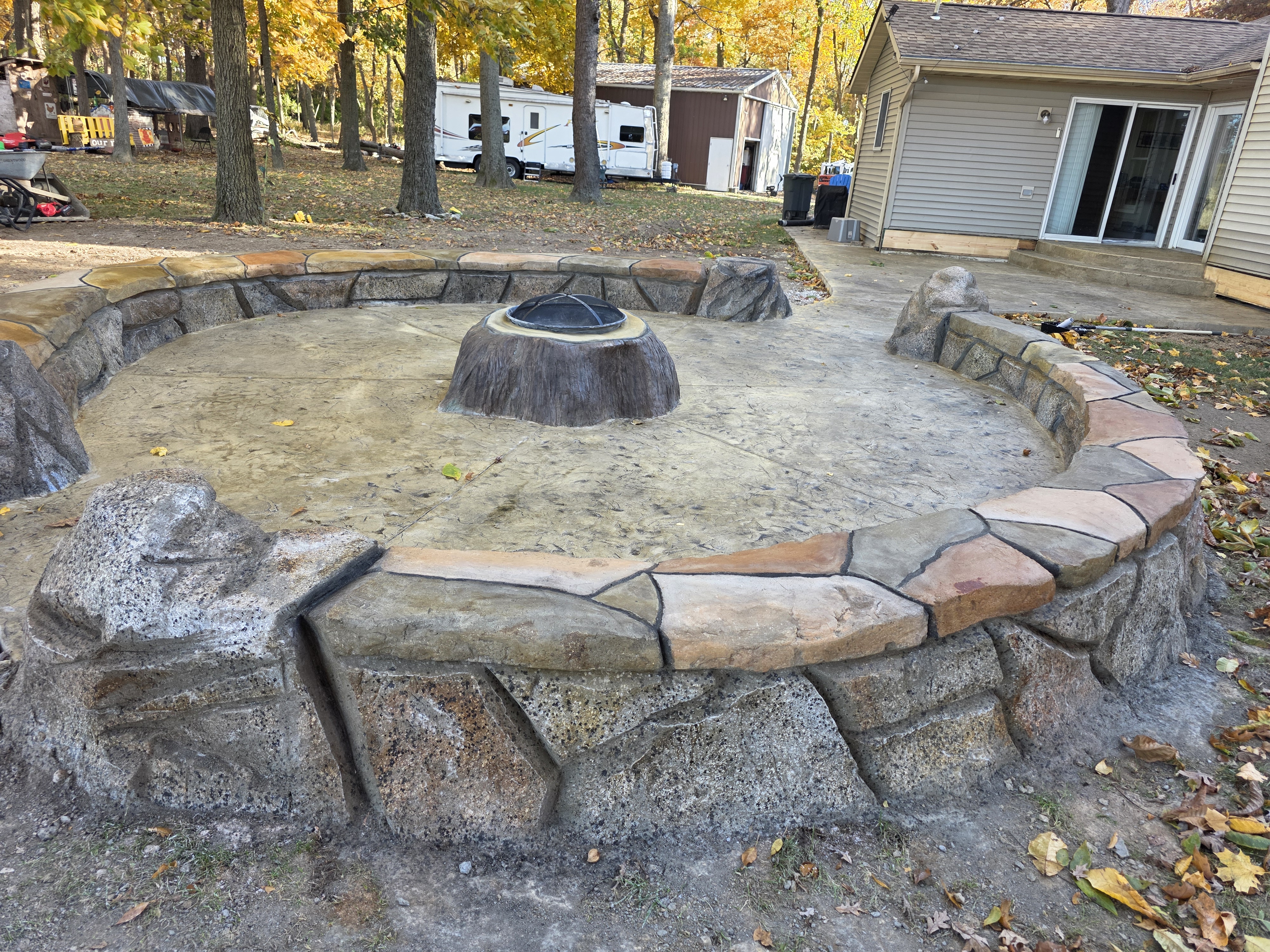 Round carved stone-look seating wall around a fire pit patio