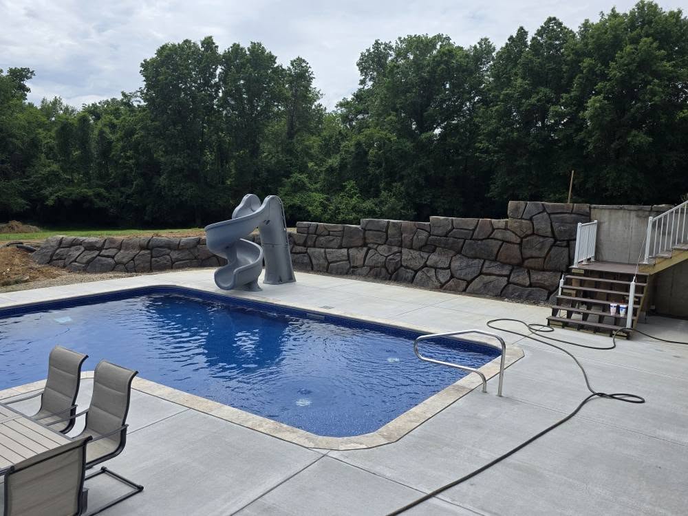 Carved stone retaining wall behind an inground pool deck
