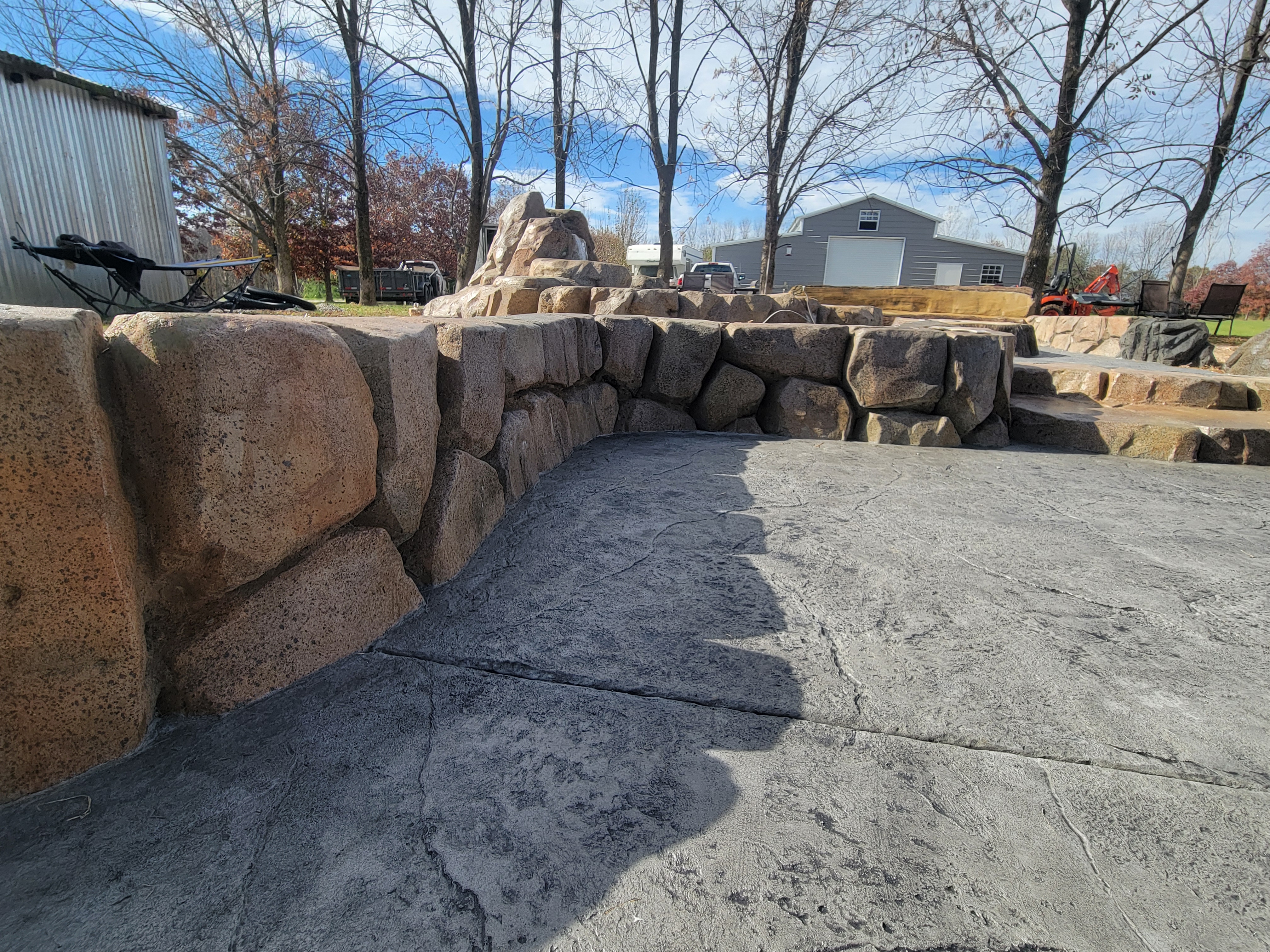Long carved boulder wall bordering a stamped concrete patio